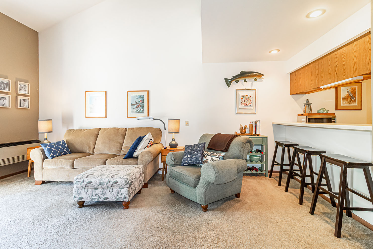 A brightly lit apartment living room with stools along a bar that faces into the kitchen