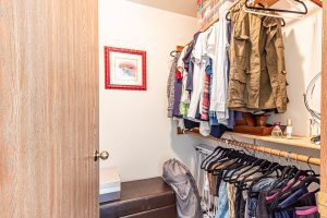 A walk in closet with men's clothing hanging up, a photo of a cat on the wall, and a leather bench