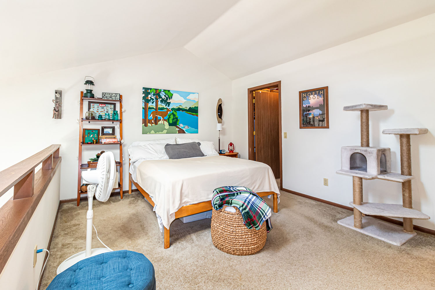 An apartment loft bedroom with a bed, bookshelf, fan, and cat tree