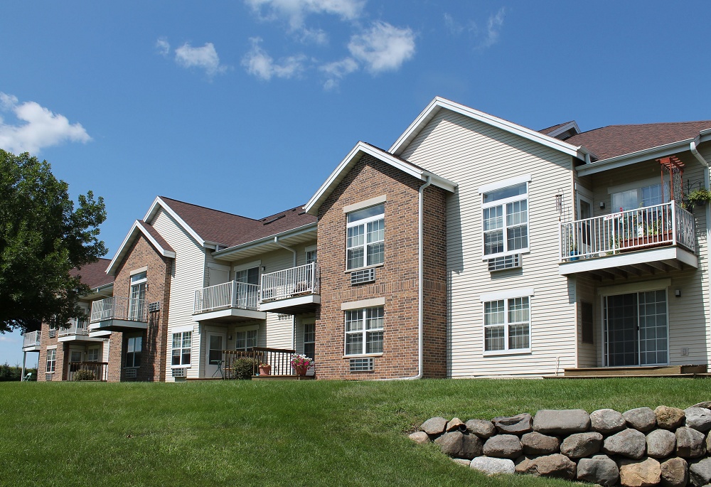 Apartment complex lawn with large rock wall on the right and trees on the left