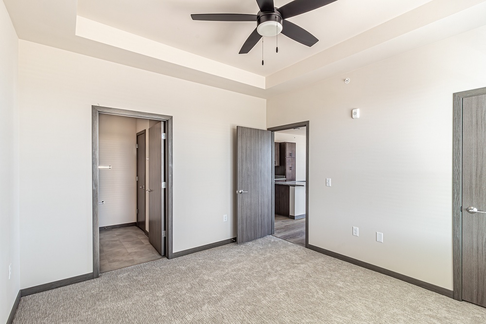 An empty apartment bedroom with a ceiling fan and various doors