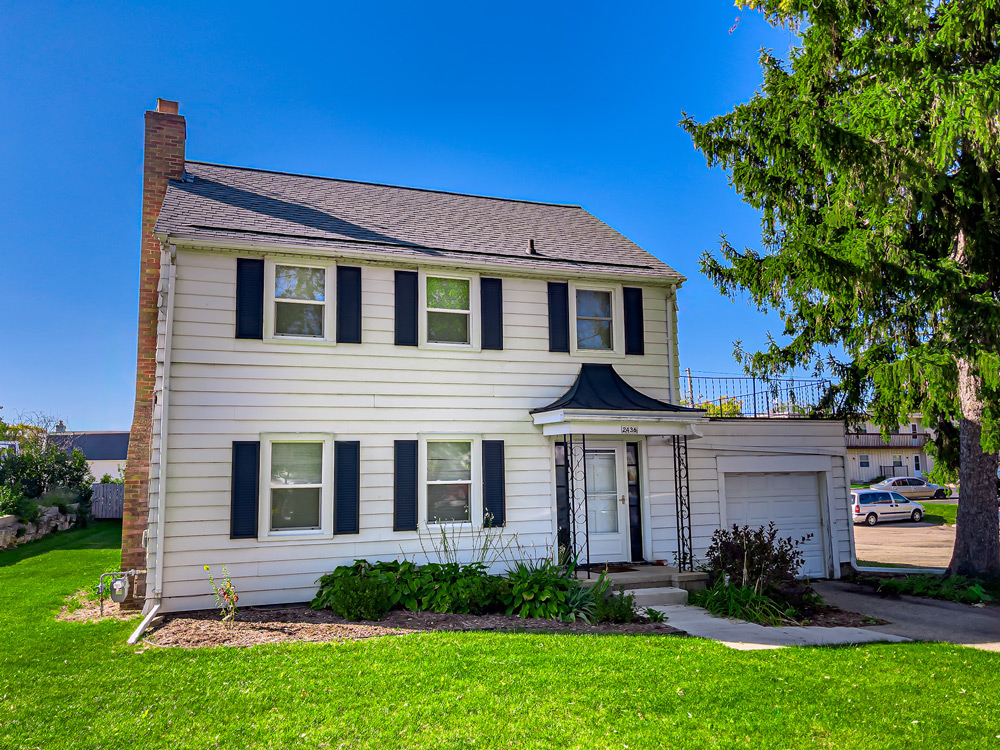 The front of a two story house with attached garage and a pine tree