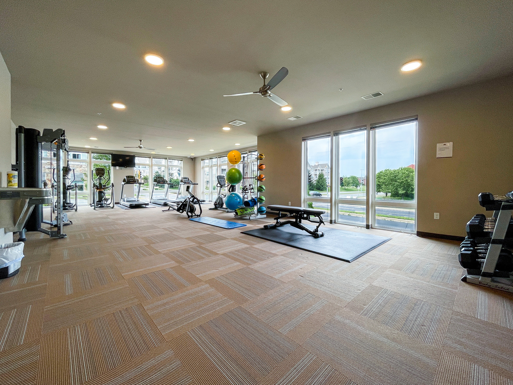A gym area with floor to ceiling windows and various workout equipment around the room