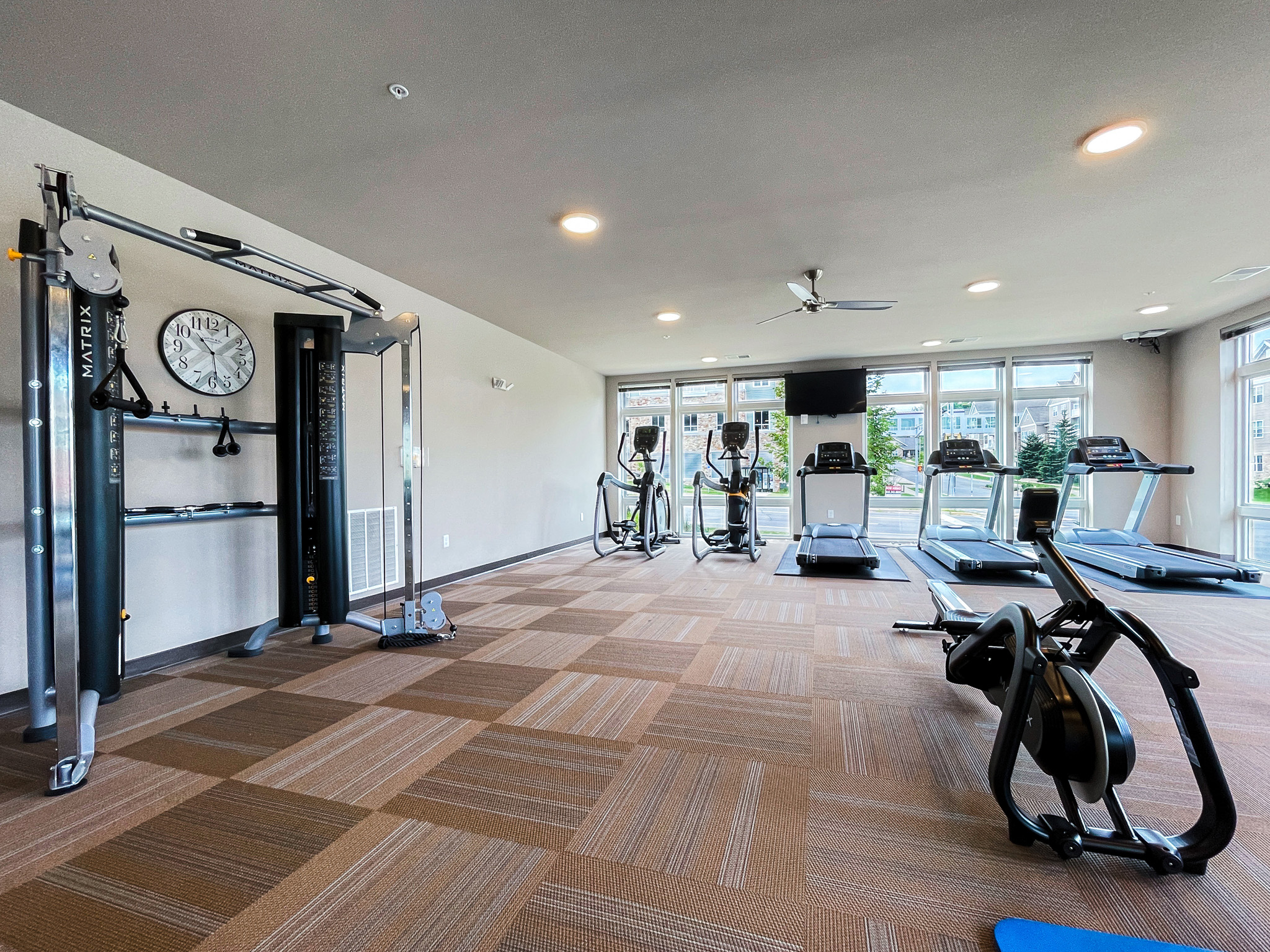 A gym area with floor to ceiling windows and various workout equipment around the room