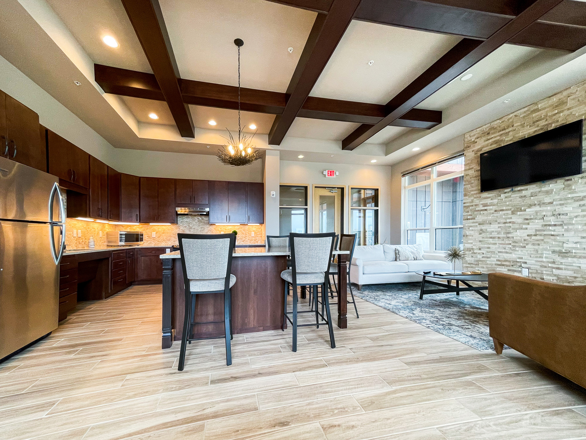 An apartment clubhouse kitchen area with an island surrounded by chairs in the center and two couches and coffee table off to the left