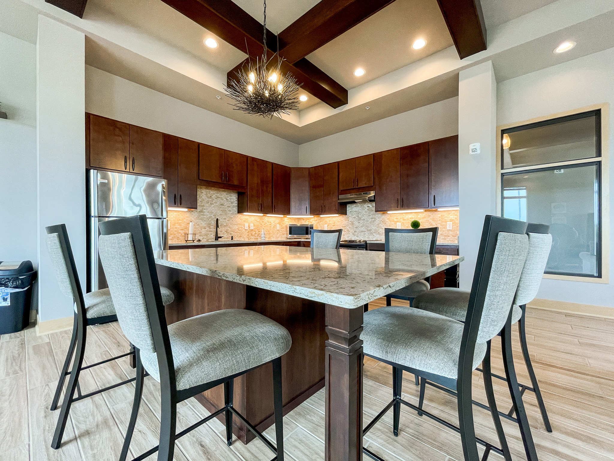 An apartment clubhouse kitchen area with an island surrounded by chairs in the center