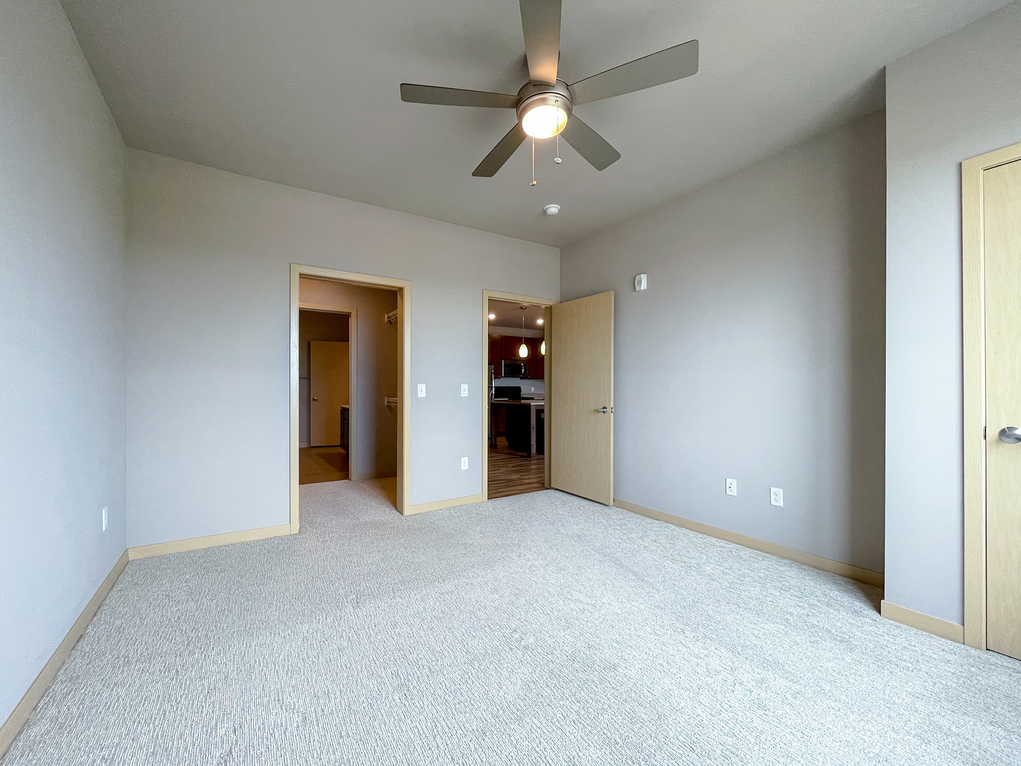 Empty apartment bedroom with ceiling fan and a door to kitchen on right and door to closet and bathroom on left