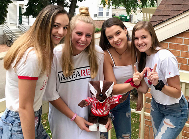 Four young women college students with one holding a Bucky Badger stuffed animal and two making a W with their fingers