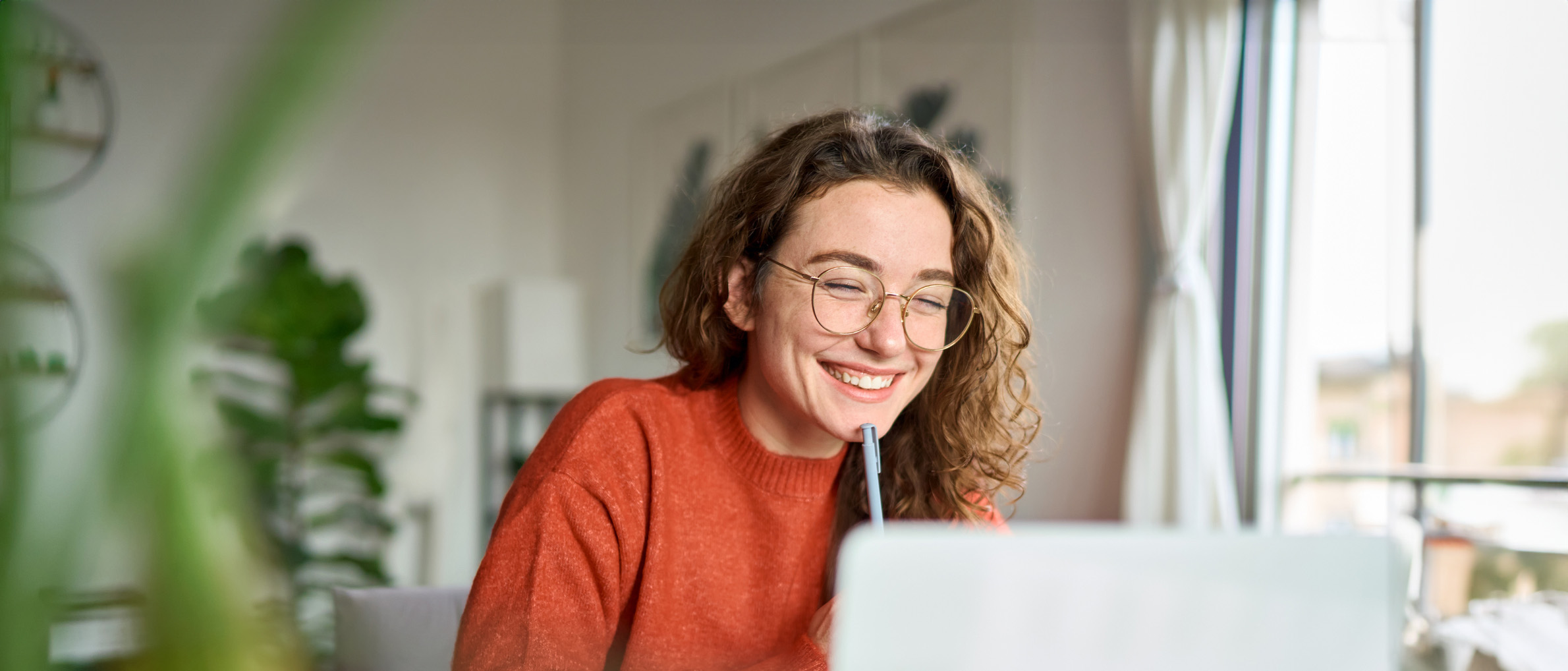 Happy young woman using laptop sitting at desk writing notes while watching webinar, studying online, looking at pc screen learning web classes or having virtual call meeting remote working from home.