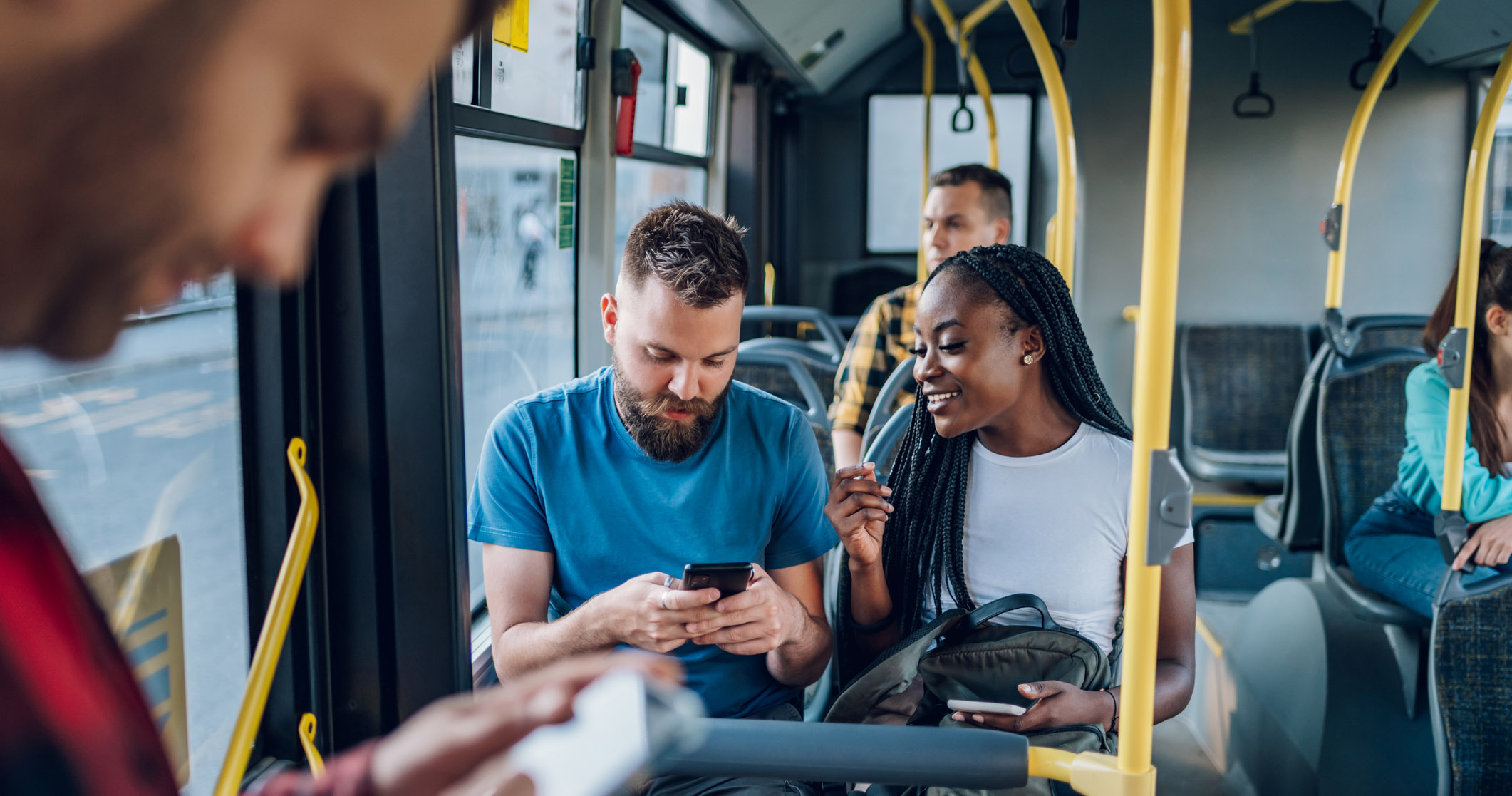 Happy multiracial couple of friends sitting in a bus and using a smartphone to message their friends who they are going to meet. Public transportation. Diverse romantic couple riding a bus.